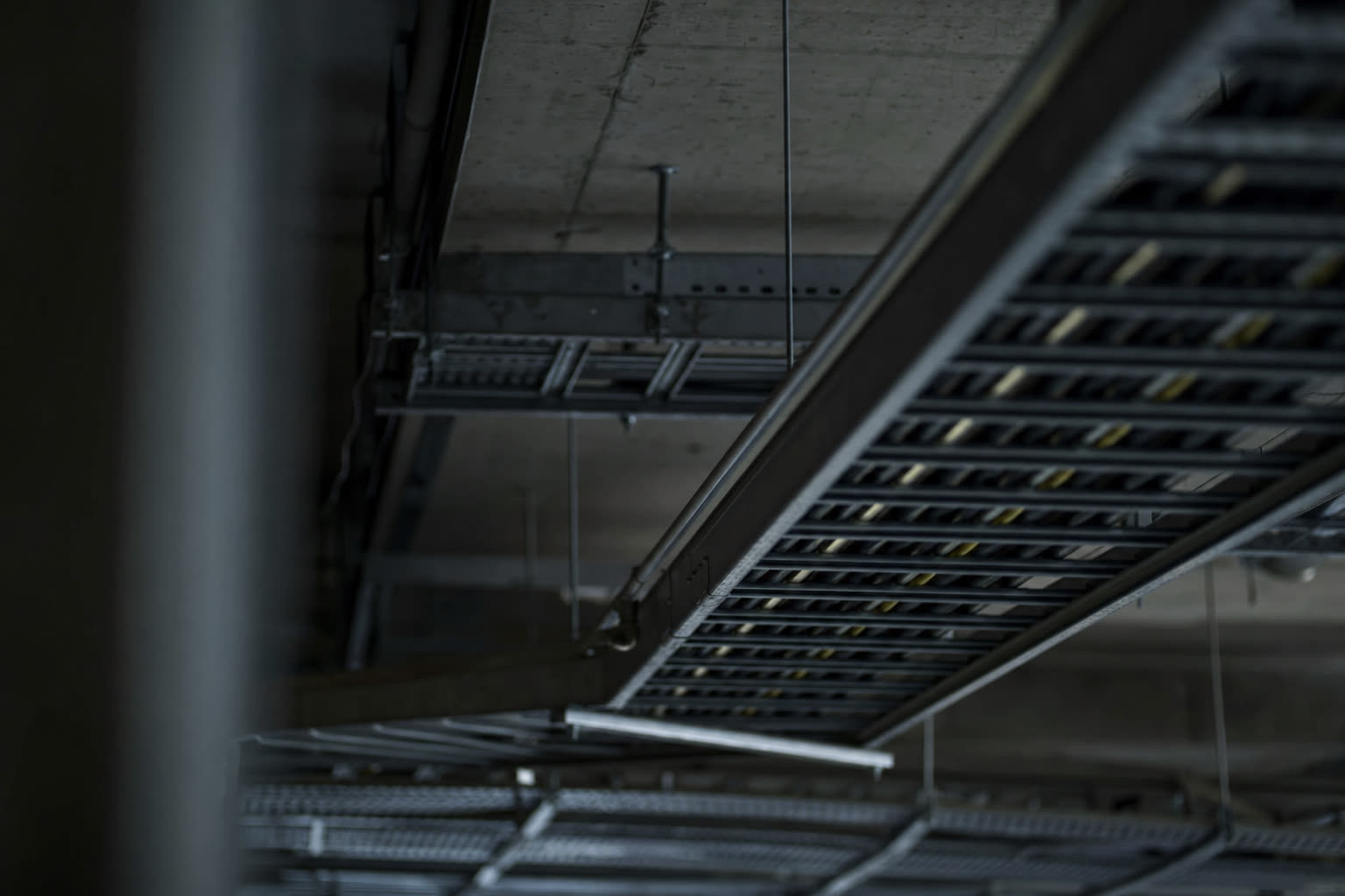 Construction cable trays and overhead conduit runs receding into shadow.